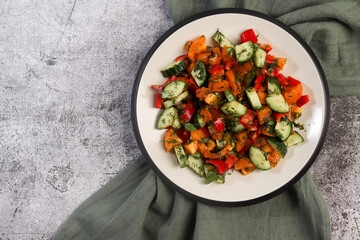 Healthy Cucumber Salad with Tomatoes, Pink Onions, Bell peppers and quail eggs on a round plate on a dark background. Top view, flat lay