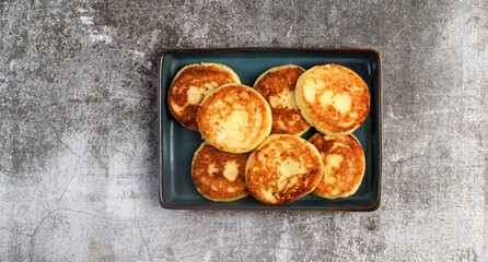 Rustic cottage cheese pancakes on a rectangular  plate on a dark background. Top view, flat lay