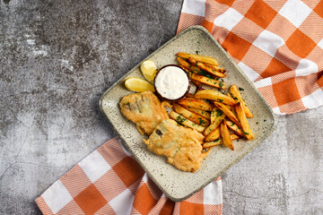 Fish and chips with sauce and lemon slices on a square  plate on a dark background. Top view, flat lay