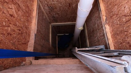 Man on the bottom of hole digging sand into bucket and then other man on top using manual crank lever to rise them up. Working on home made water well next to mobile house.