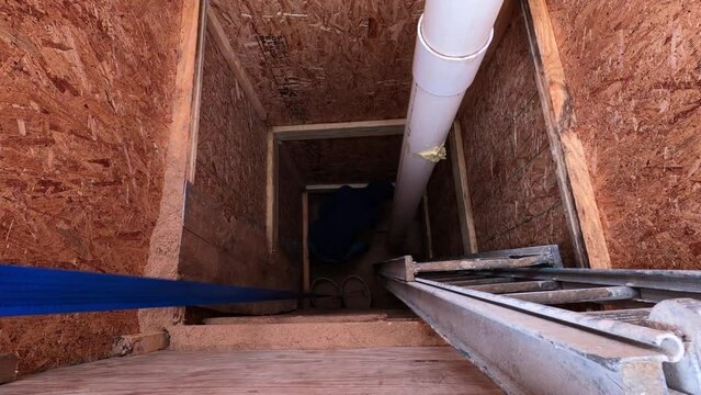 Man on the bottom of hole digging sand into bucket and then other man on top using manual crank lever to rise them up. Working on home made water well next to mobile house.
