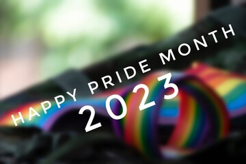 Happy Pride Month 2023 with blurred rainbow wristband and flag background, concept for LGBT community celebrations in pride month, June, around the world. - obrazy, fototapety, plakaty