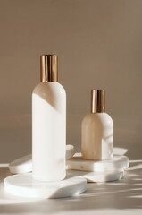 Natural cosmetic skincare bottles mockup on marble podium and sunlight shadow on brown background . Product presentation. Beauty and body care product concept. Neutral beige colors. Copy space.