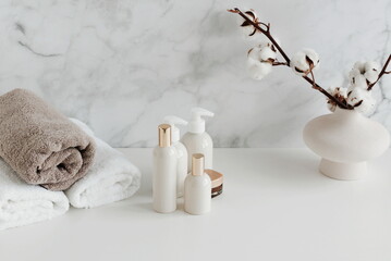 Spa, bathroom background. Towels and cosmetic products mockup on white desk near marble wall and interior accessories. copy space.  Neutral beige colors.toned