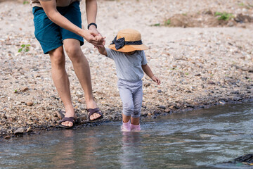 Father and adorable daughter relationship concept, man and kids spent free time in national park on holiday, father holds little hand of daughter for safety walking cross the small stream in park