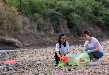 Asian woman pick up dirty plastic in the stream for recycling. Two female volunteer to collect rubbish around the beach in a campaign to reduce global warming. Causes of death of aquatic animals.