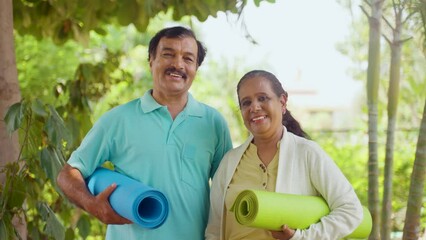 Happy smiling indian senior couple with yoga mat looking at camera during morning workout at park - concept of fitness, active healthy lifestyle and wellness. - Powered by Adobe