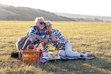 Obraz premium Senior couple enjoying a delightful picnic. The couple has a relaxed and contented expression as they share a bottle of wine and a delicious spread of food.