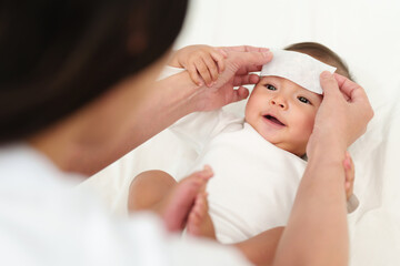 Obraz na płótnie Canvas mother putting cool fever pad on forehead of happy sick baby