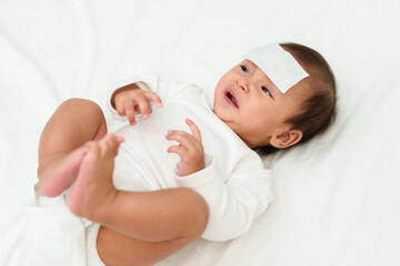sick crying baby with cool fever pad on forehead