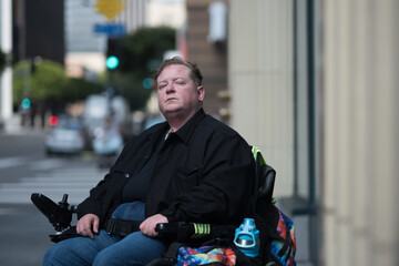 A disabled transman on a busy sidewalk takes a moment to look directly at the camera, pausing...