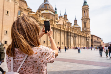 Fototapeta premium Tourist woman taking a photo with the mobile phone to the cathedral basilica del Pilar in Zaragoza, Spain.