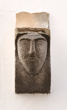 Ancient carved stone face on facade in Evora town