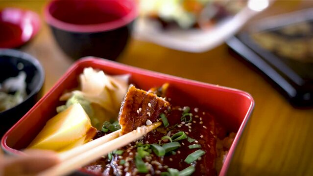 Asian men hands are using chopsticks, to pick eel rice or, Unaju Japanese food put it in a square-shaped box, Jubako, and eat it with kimosui. or eel offal soup cuisines Asia japan food