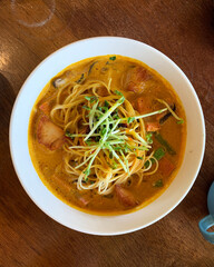 home cook laksa spicy coconut chili curry sauce paste soup with noodle mee pasta and vegetables in bowl on cafe wood table top view asian local halal food vegan menu