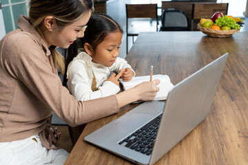 Beautiful mother teaching her lovely daughter to do homework in living room