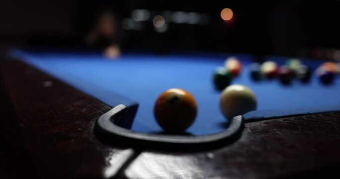 White billiard ball strikes yellow on blue billiard table. Person hits billiard ball using cue and misses hole in club dark playing room