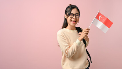 Cheerful young Asian woman showing a Singapore flag on pink isolated background