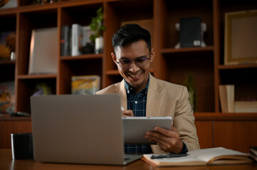 Professional adult Asian businessman using his tablet to manage his tasks at his desk