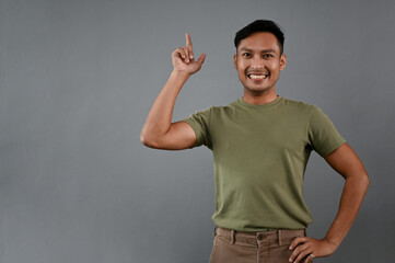 Smiling Asian man pointing his finger up while standing on an isolated grey background.