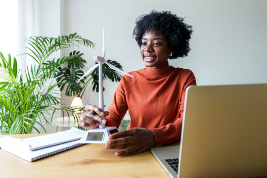 Smiling businesswoman with model wind turbine sitting at desk