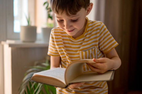 Smiling boy flipping pages of book at home - Powered by Adobe