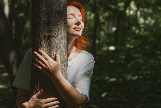 Woman embracing tree in forest at sunny day