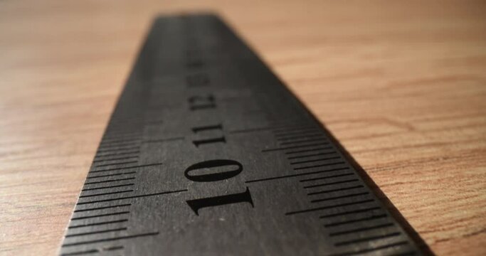 Metal ruler with digits and lines for measuring length on wooden table. Repairer of premises tool on desk in room. Manual foreman instruments