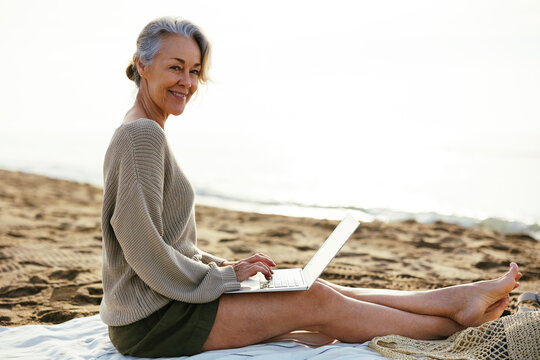 Smiling woman with laptop sitting at beach