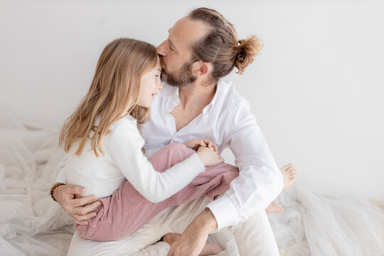 Father kissing daughter sitting near white wall