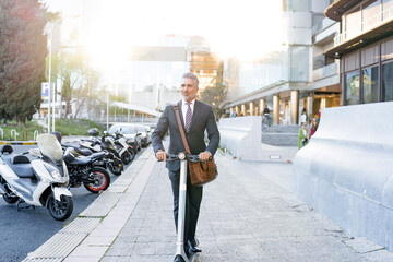 Businessman riding electric scooter on sidewalk at sunny day