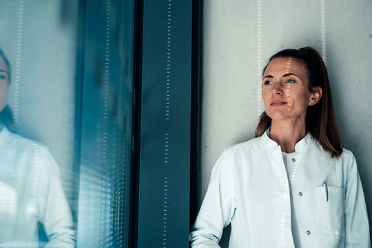 Thoughtful doctor wearing lab coat standing near wall at hospital