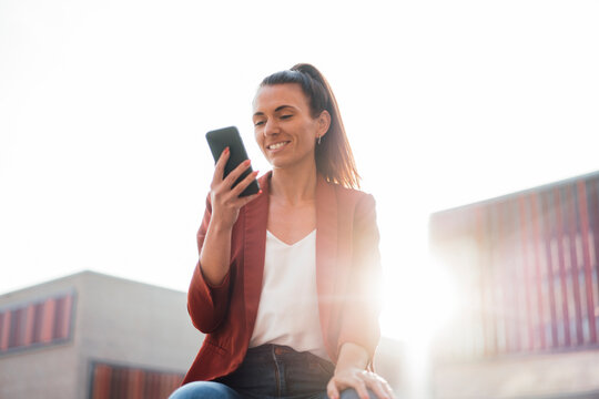 Smiling businesswoman text messaging through smart phone at sunny day