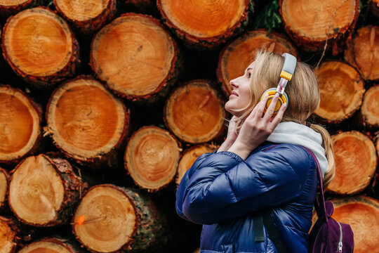 Smiling young woman listening music through headphones by stack of logs