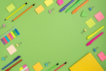 Frame of colorful school and office stationery set on green background. Flatly.