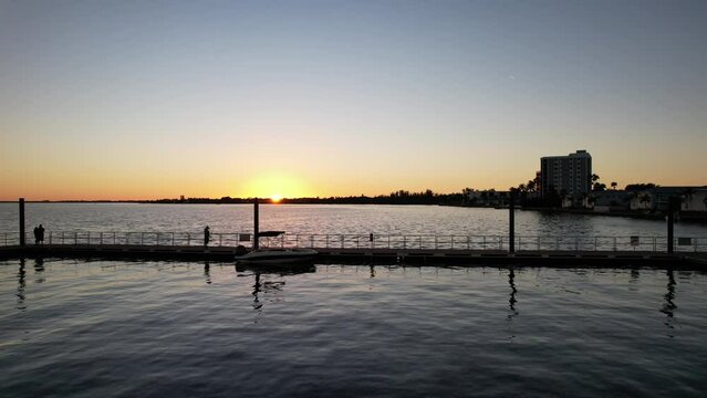 On the shore next to the city, reflecting the bright sunlight, there is a wonderful panoramic view of the sunset over the smooth water surface.