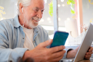 Fototapeta premium Smart work concept. Smiling senior man in coffee shop while working on laptop talking on phone. Elderly man people enjoying free lifestyle doing job from remote