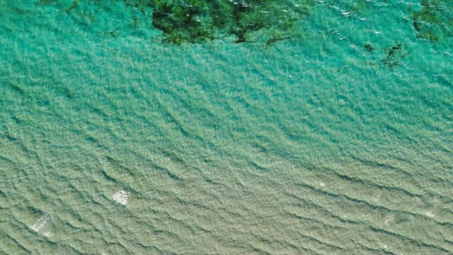 Top down aerial of turquoise teal sea waves crashing against summer beach