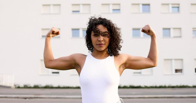 Young woman flexing muscles in front of buiilding