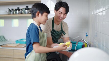 Asian boy helping father washing dish in kitchen at home on holiday. Single father, Happy family in kitchen
