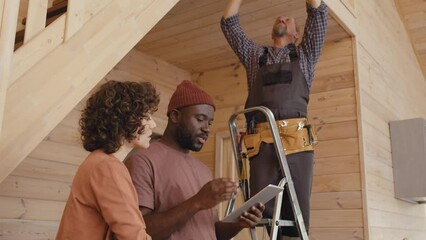 African American specialist teaching female client how to use home automation system while his Caucasian colleague setting sensor