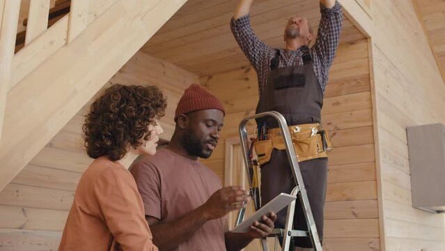 African American specialist teaching female client how to use home automation system while his Caucasian colleague setting sensor