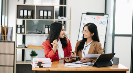 Two Asian businesswoman discuss investment project working and planning strategy with tablet laptop computer in office.