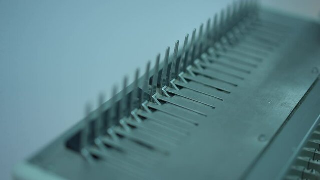 Close-up office comb binding machine with rack focus moving along combs. Device for bind pages together into a book indoors closeup