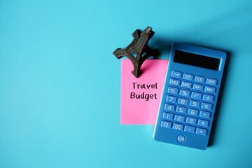 Mini Eiffel model,calculator,pen on blue copy space background with pink note written TRAVEL...