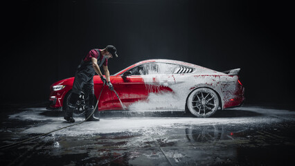 Car Wash Specialist Using Pressure Washer to Rinse a Red Modern Sportscar. Adult Man Washing Away...
