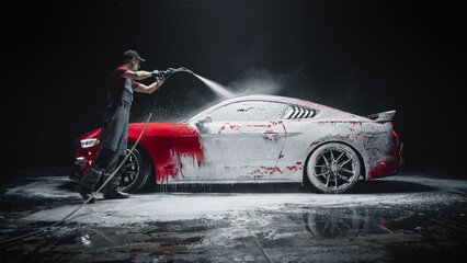 Car Wash Expert Using Water Pressure Washer to Clean a Red Modern Sportscar. Adult Man Washing Away...