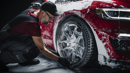 Car Ad Style Photo of a Professional Car Wash Specialist Using a Big Soft Sponge to Wash the Rims of a Beautiful Red Sportscar with Shampoo Before Detailing, Polishing and Waxing