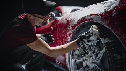 Red Sportscar's Wheels Covered in Shampoo Being Rubbed by a Soft Sponge at a Stylish Dealership Car Wash. Performance Vehicle Being Washed in a Detailing Studio