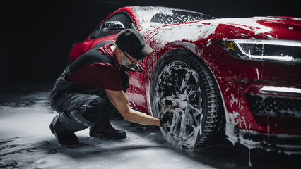 Red Sportscar's Wheels Covered in Shampoo Being Rubbed by a Soft Sponge at a Stylish Dealership Car...